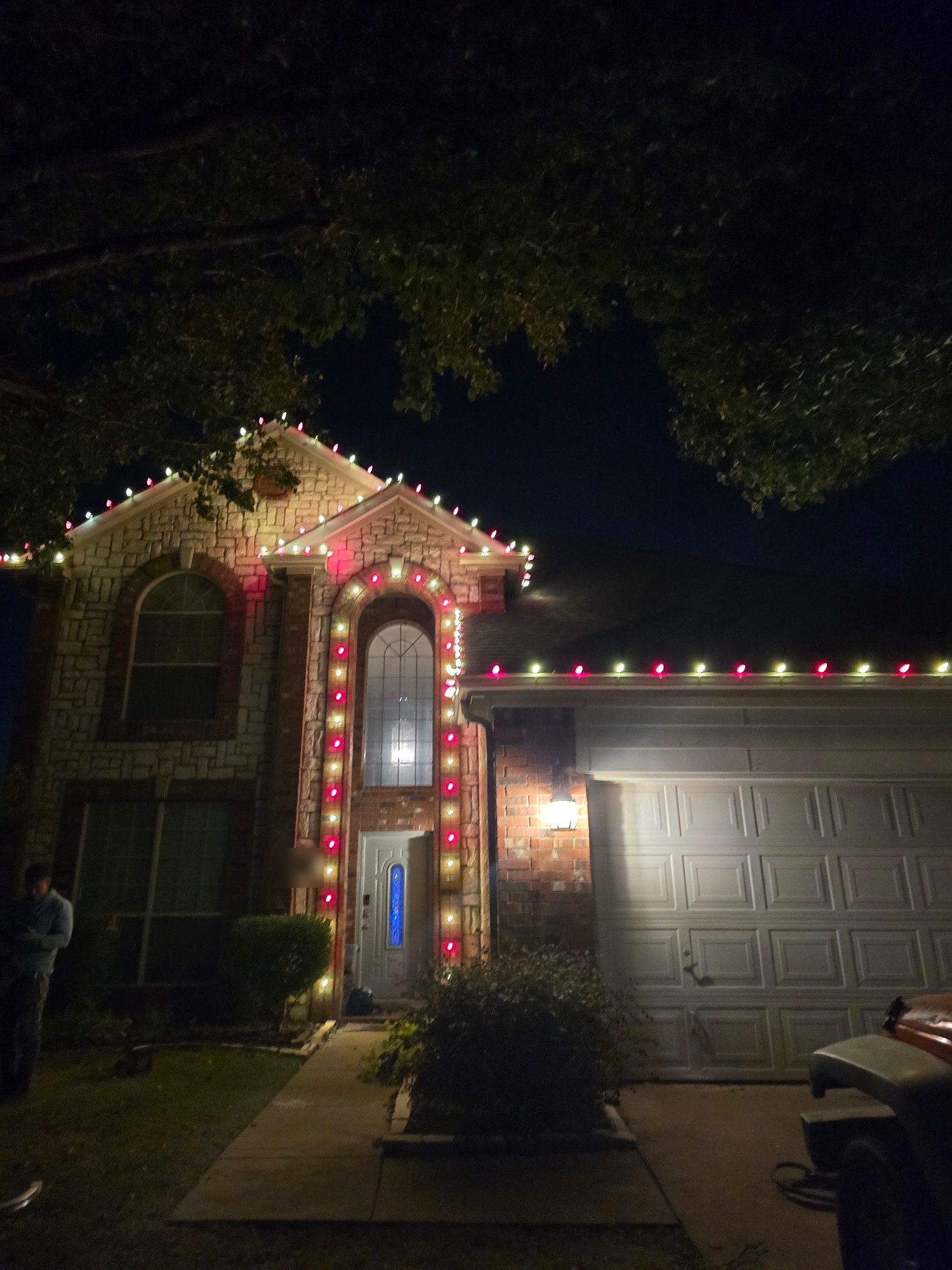 Two-story stone house outlined in red and white lights along the roof and around the tall front entry