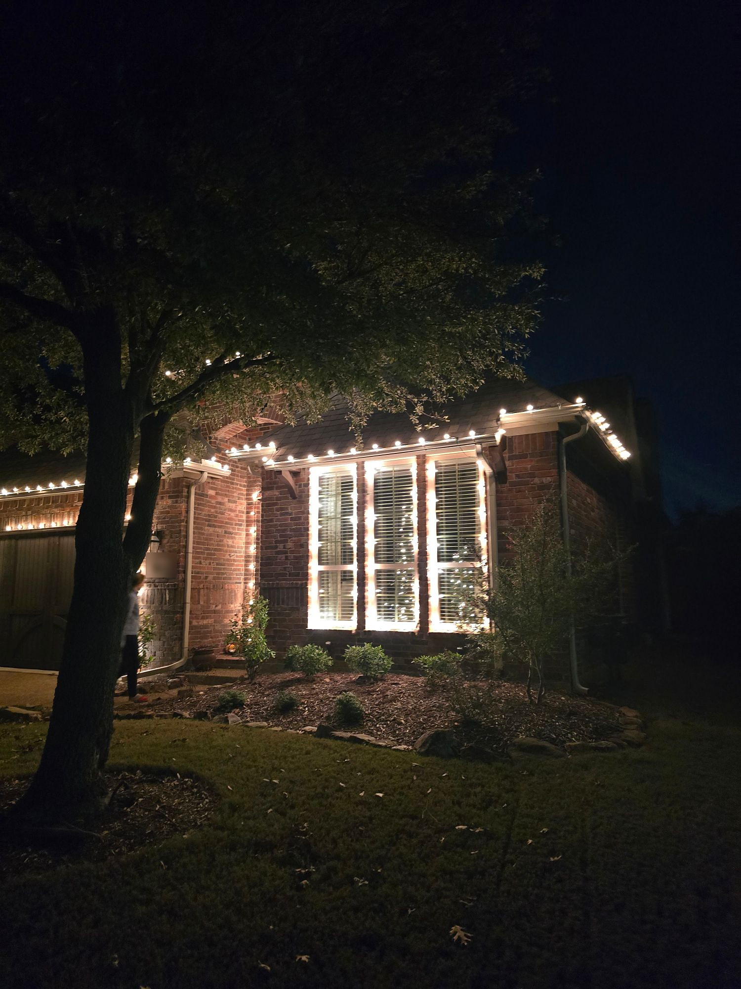Brick house with warm white lights along the roofline and framing the front windows